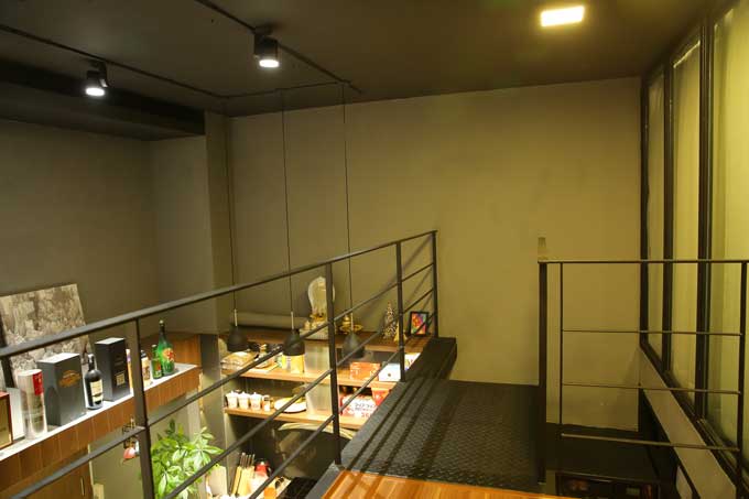 Cầu thang dẫn lên gác lửng sơn màu đen và khoảng không tiếp nối giữa hai tầng được chủ nhân trưng dụng để làm kệ trưng bày rượu.