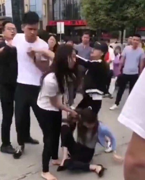 Anh chồng (áo phông trắng) lao vào can vợ đánh bồ nhưng bị người đi đường (mặc áo đen) chỉ tay vào mặt mắng mỏ. Ảnh cắt từ video.
